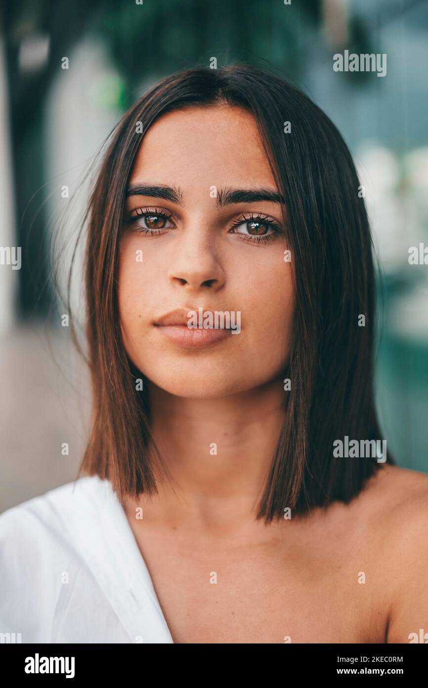 Glückliche junge modische Frau mit kurzen Haaren, die im Freien auf die Kamera schaut. Schöne zufriedene Dame mit kurzen Haaren lächelnd, während sie der Kamera gegenübersteht. Porträt einer selbstbewussten weiblichen Jugend lächelnd Stockfoto