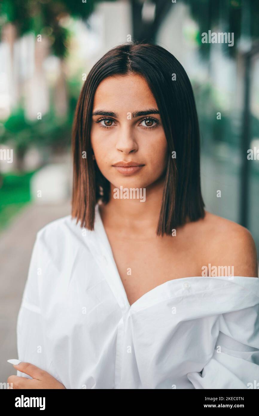 Glückliche junge modische Frau mit kurzen Haaren, die im Freien auf die Kamera schaut. Schöne zufriedene Dame mit kurzen Haaren lächelnd, während sie der Kamera gegenübersteht. Porträt einer selbstbewussten weiblichen Jugend lächelnd Stockfoto