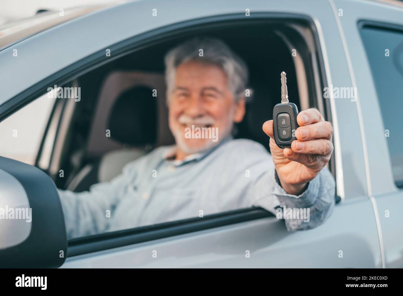 Porträt eines glücklichen alten Mannes, der der Kamera die Autoschlüssel des Autos zeigt. Zufriedener Kunde, der sein neues Auto genießt. Stockfoto
