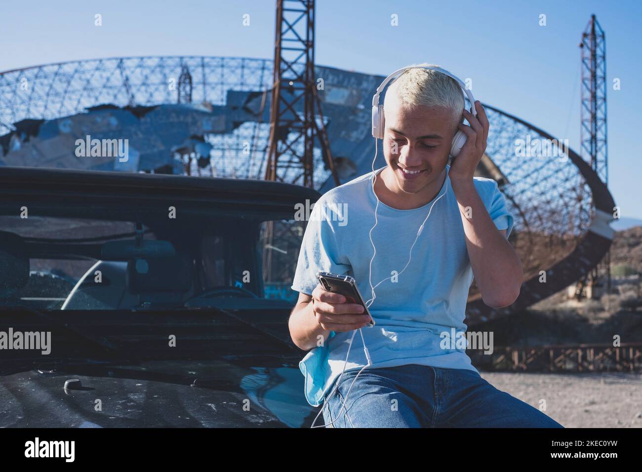 Ein Teenager oder kaukasischer Mann, der sein Telefon und Gerät allein auf seinem Auto benutzt - technologieabhängiges Konzept und Online-Lifestyle - Reisende im Urlaub, der sich die Karten seines Tablets anschaut Stockfoto