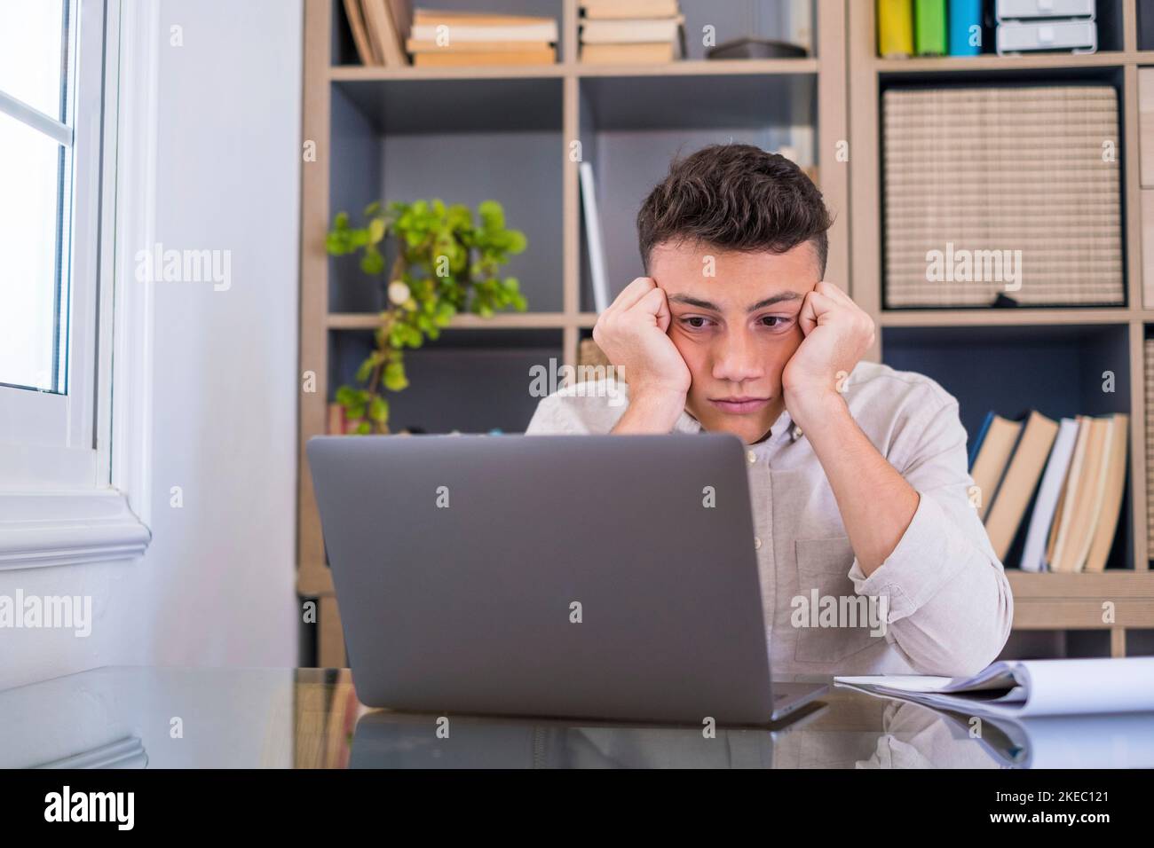 Müde männliche Student oder Arbeiter sitzen zu Hause Schreibtisch Blick in der Ferne Schlafentzug, faul Millennial Mann abgelenkt von der Arbeit fühlen faul Mangel an Motivation, denken an langweilige monotone Arbeit Stockfoto