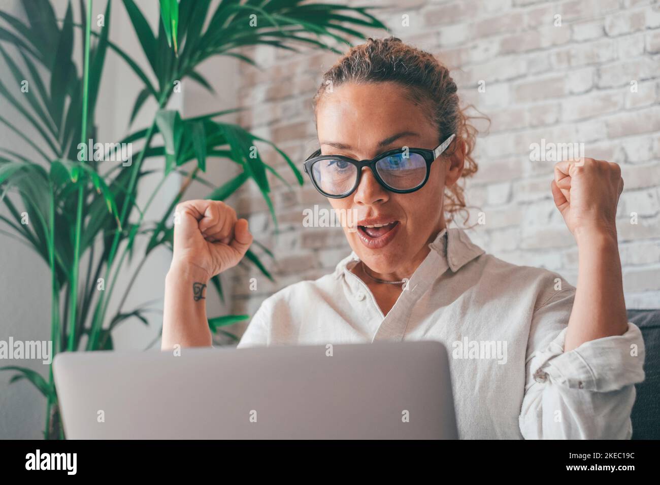 Frau sitzt auf dem Sofa PC auf den Schoß geballte Fäuste brüllen vor Freude, während sie auf dem Laptop gute Nachrichten lesen. Spieler feiern den Sieg bei Online-Auktionen. Bekam unglaubliche Angebot aufrichtige Emotionen des Glücks Konzept Stockfoto