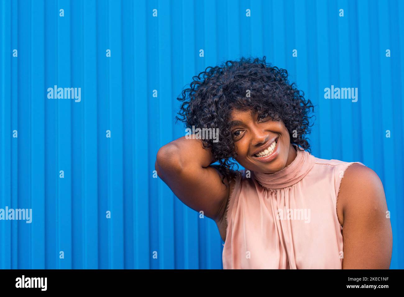 Farbenfrohes Porträt einer jungen afrikanischen und amerikanischen Frau, die lächelt und die Kamera anschaut, mit blauen, schönen Farben Stockfoto
