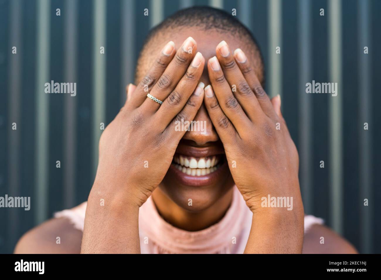 Porträt einer jungen und fröhlichen schwarzen afrikanischen oder amerikanischen Frau, die mit ihren Händen auf den Augen die Kamera anlächelt Stockfoto