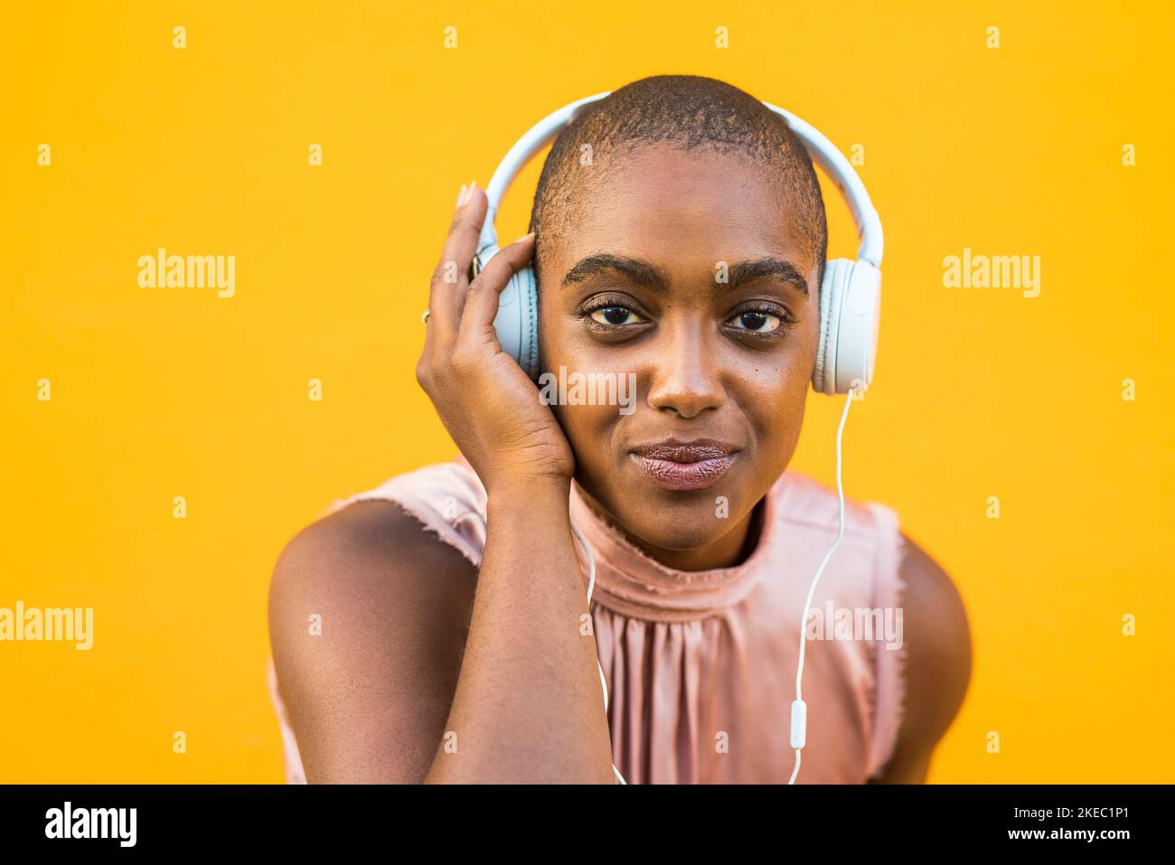 Porträt einer dunkelhäutigen Frau, die auf einem Kopfhörer auf gelbem Hintergrund Musik hört. Lächelnde afroamerikanische Dame, die ihr Lieblingslied mit kabelgebundener Audioausrüstung genießt. Technologie und Unterhaltung Stockfoto