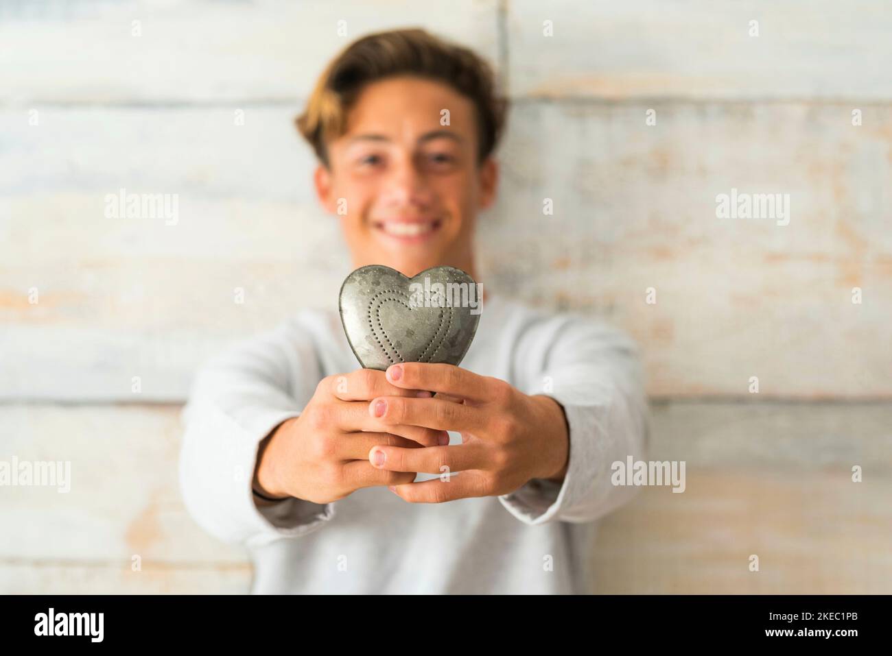 Nahaufnahme eines Teennagers, der zu Hause ein Metallherz hält Mit einem hölzernen Hintergrund - oy gibt sein Herz concpet Stockfoto