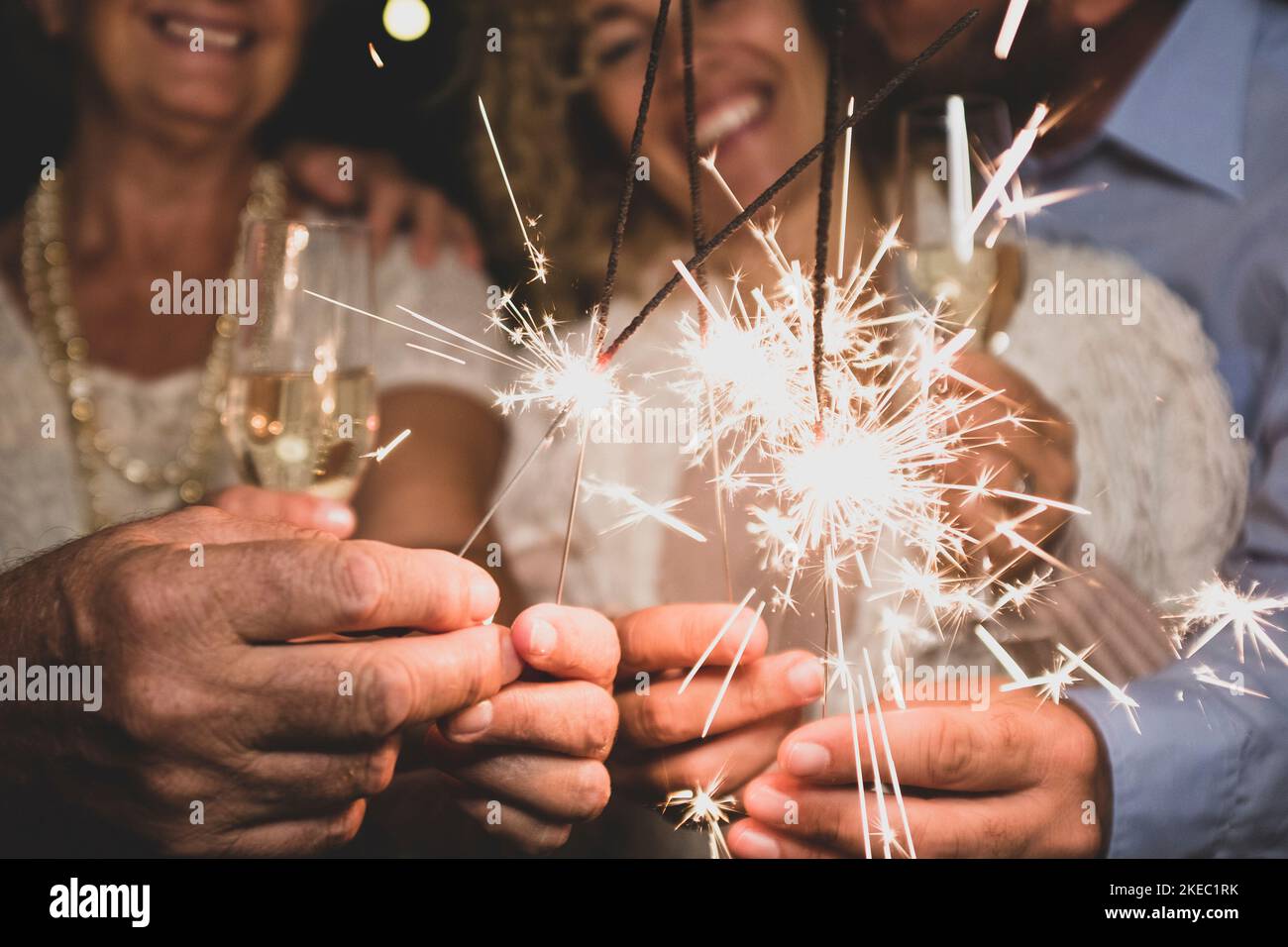 Eine Gruppe von vier Personen genießt die Neujahr-Nacht, feiert mit Wunderkerzen in der Mitte und schaut auf die Kamera - Erwachsene haben Spaß zusammen Stockfoto