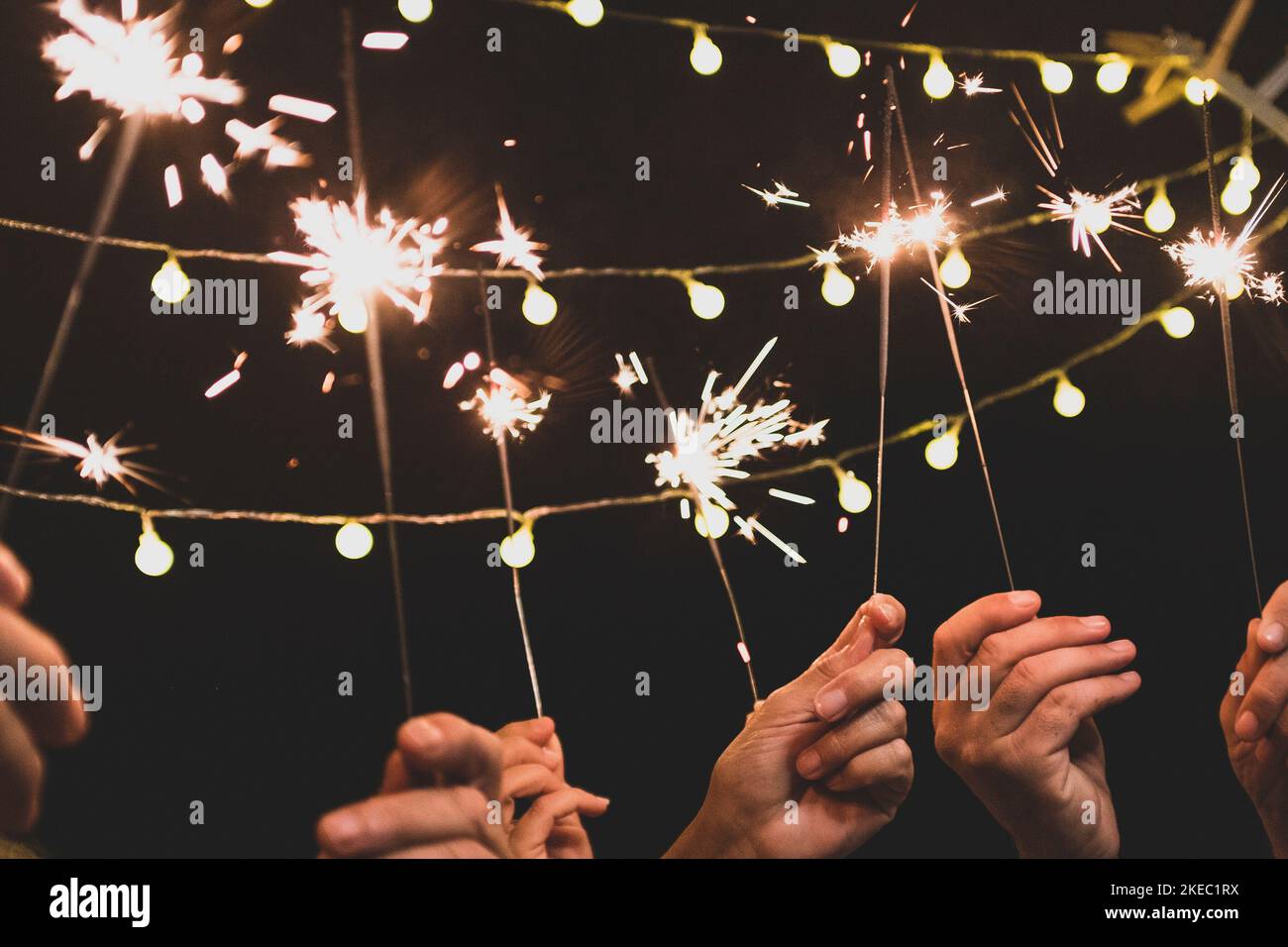 Eine Gruppe von vier Personen genießt die Neujahr-Nacht, feiert mit Wunderkerzen in der Mitte und schaut auf die Kamera - Erwachsene haben Spaß zusammen Stockfoto