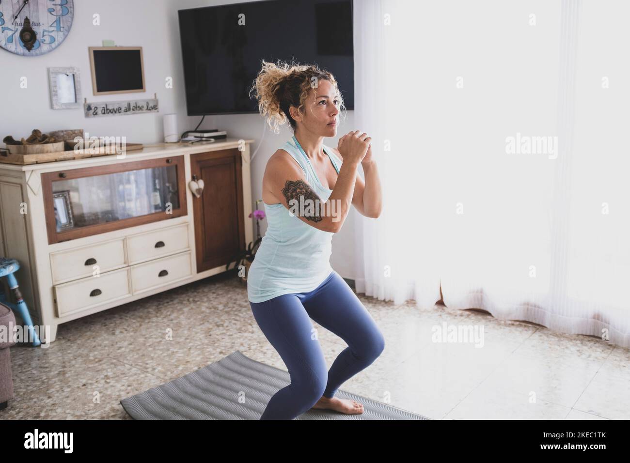 Eine junge Frau zu Hause drinnen tun Übung allein zu Sei fit und gesund - lockiges Mädchen, das Yoga macht Ihr Haus in Quarantäne und Absperrung - schöne aktive Frau Spaß haben Stockfoto