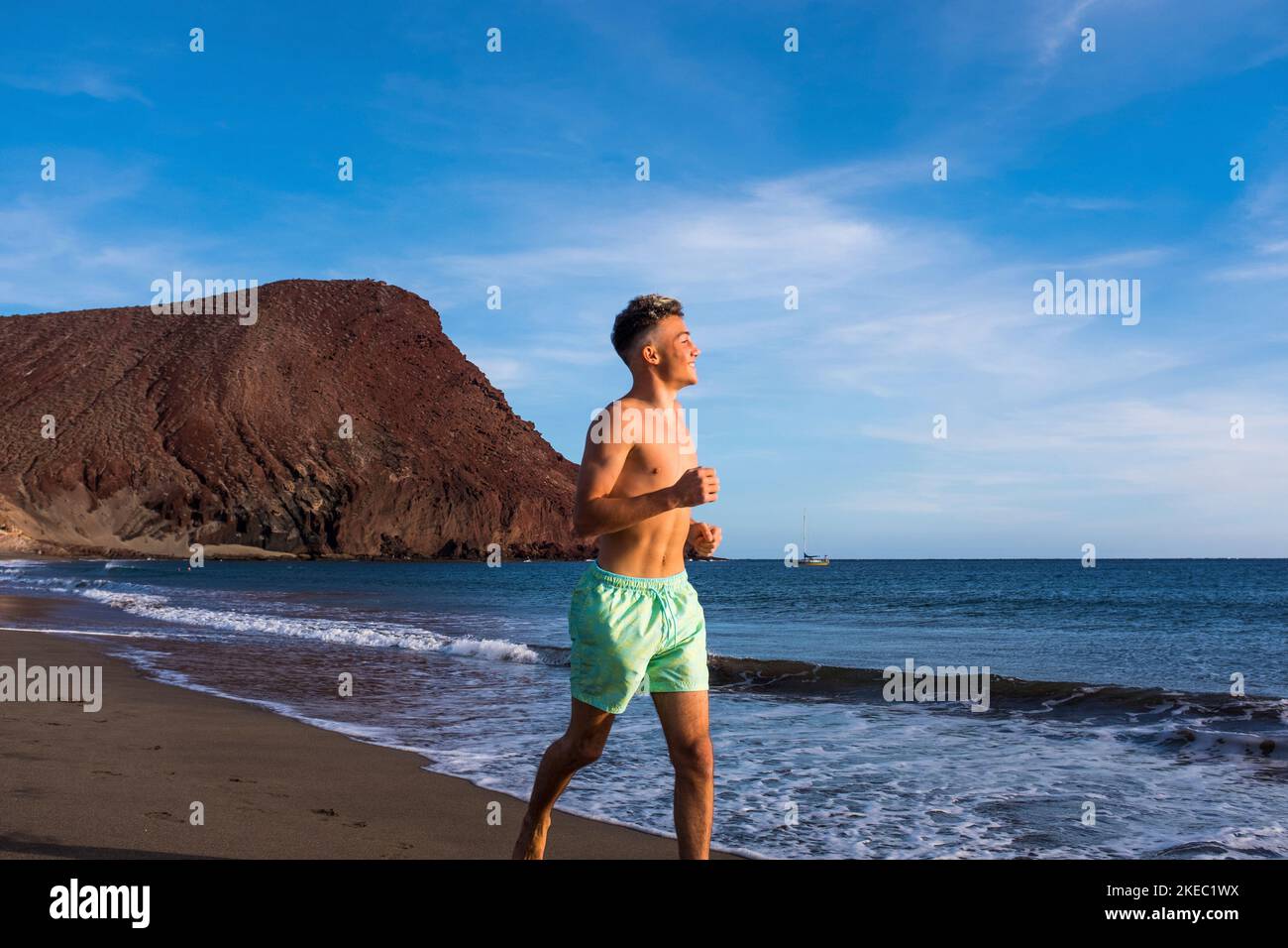 Ein Mann oder Teenager läuft auf dem Sand der Strand in der Nähe des Meeres oder des Ozeans - glücklicher und gesunder Lebensstil im Sommer in der Urlaubszeit Stockfoto
