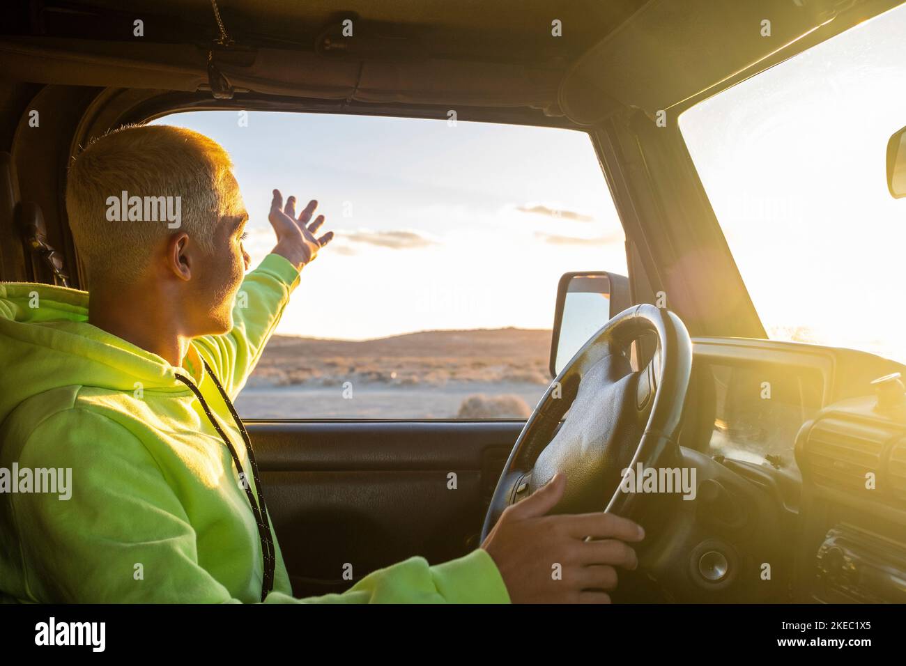 Ein junger Mann fährt mit seinem Auto und schaut auf den Sonnenuntergang, genießt seinen Urlaub und Urlaub allein im Freien - Reise- und Reisekonzept - Teenager mit Auto, das die Sonne betrachtet Stockfoto