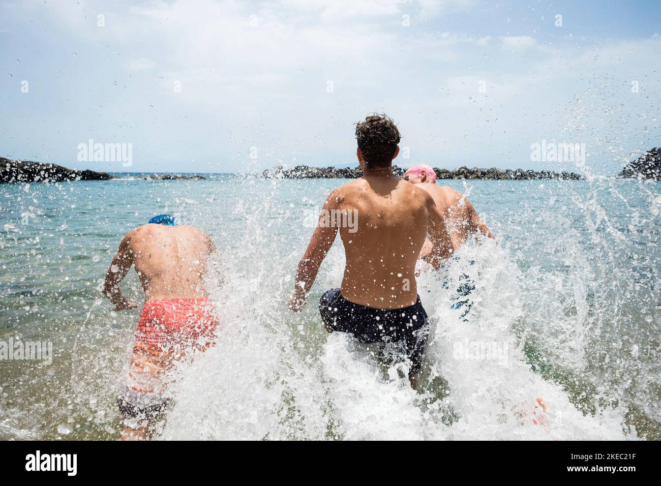 Gruppe von drei Teenagern und jungen Männern genießen Sommerferien Am Strand schwimmen und laufen zum Meer oder ocean lächelnd und lachend - glückliche Menschen mit farbigen Haaren Spaß haben Stockfoto