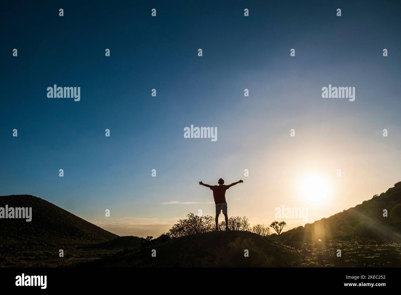 Ein isolierter und alleinstehender Mann mit offenen Armen auf einem Hügel, der den Sonnenuntergang betrachtet - ein aktives und gesundes Lebenskonzept des Gewinners - der den Horizont betrachtet Stockfoto