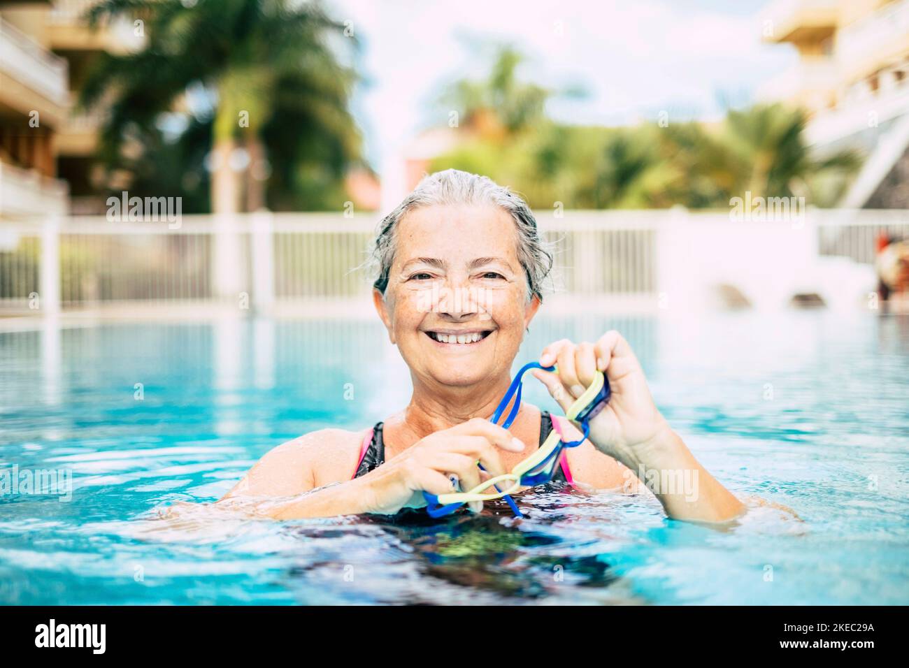 Eine reife Frau, die alleine am Pool schwimmt und trainiert, schaut auf die Kamera und lächelt Stockfoto