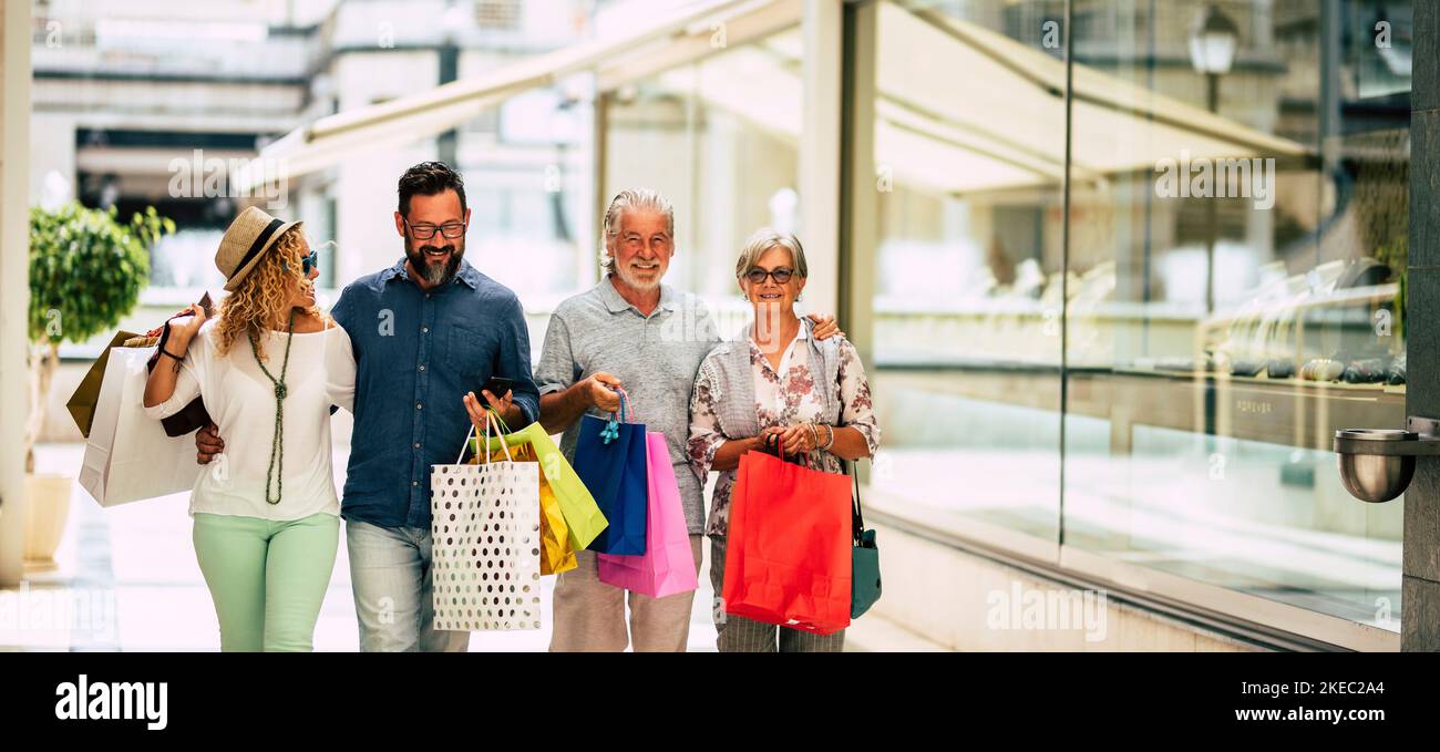Eine Gruppe von vier Personen, die zusammen einkaufen gehen und Einkaufstaschen mit Geschenken oder Geschenken zu weihnachten halten - Kleidung und mehr in einem Einkaufszentrum oder in einigen Geschäften kaufen Stockfoto