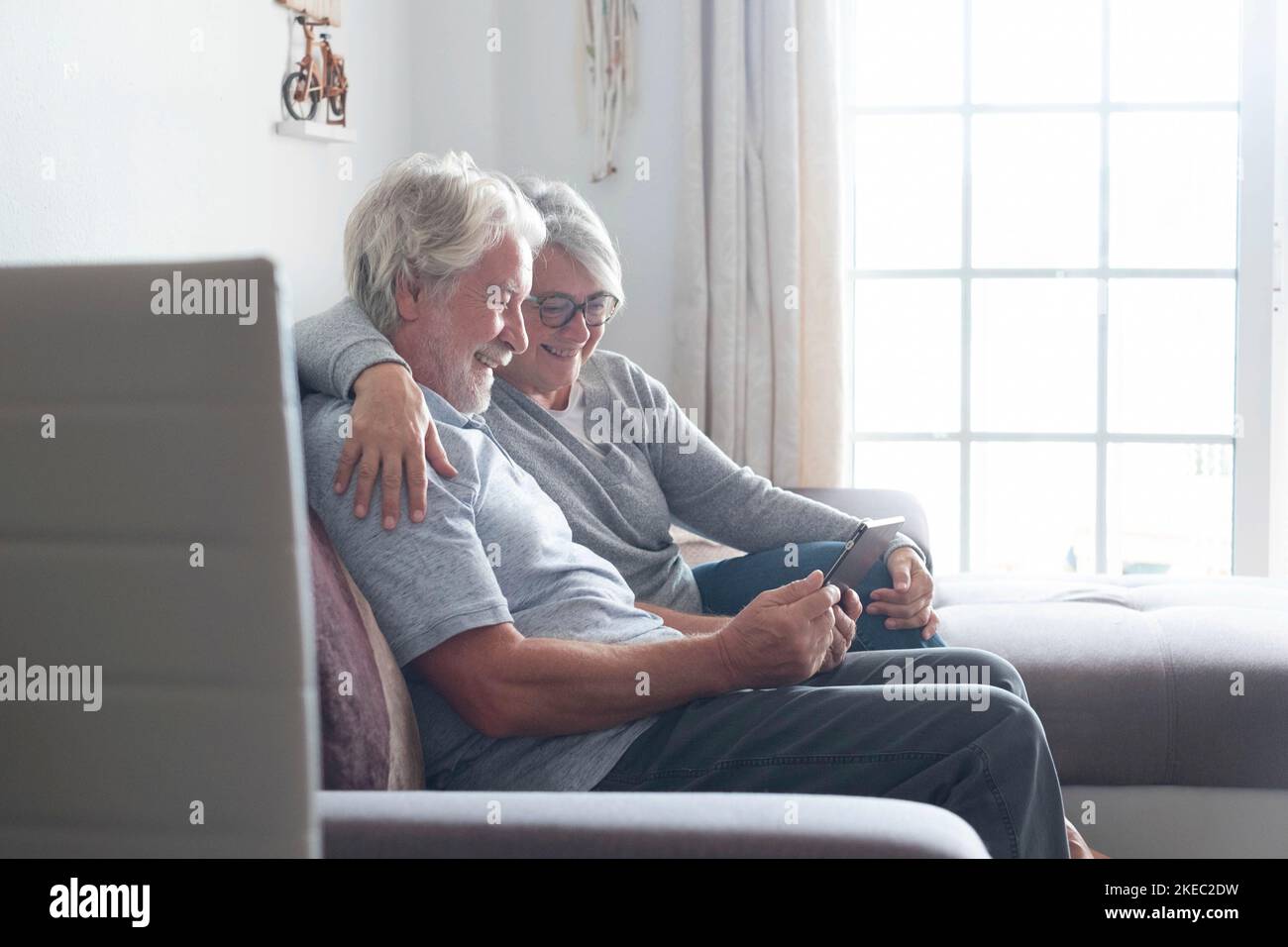 Ein paar Senioren oder ältere Menschen zu Hause auf dem Sofa, die ihr Tablet oder ihr Technologiegerät lächelnd und lachend benutzen und Videos oder lustige Fotos ansehen - mobiler und technologischer Lebensstil und Konzept Stockfoto