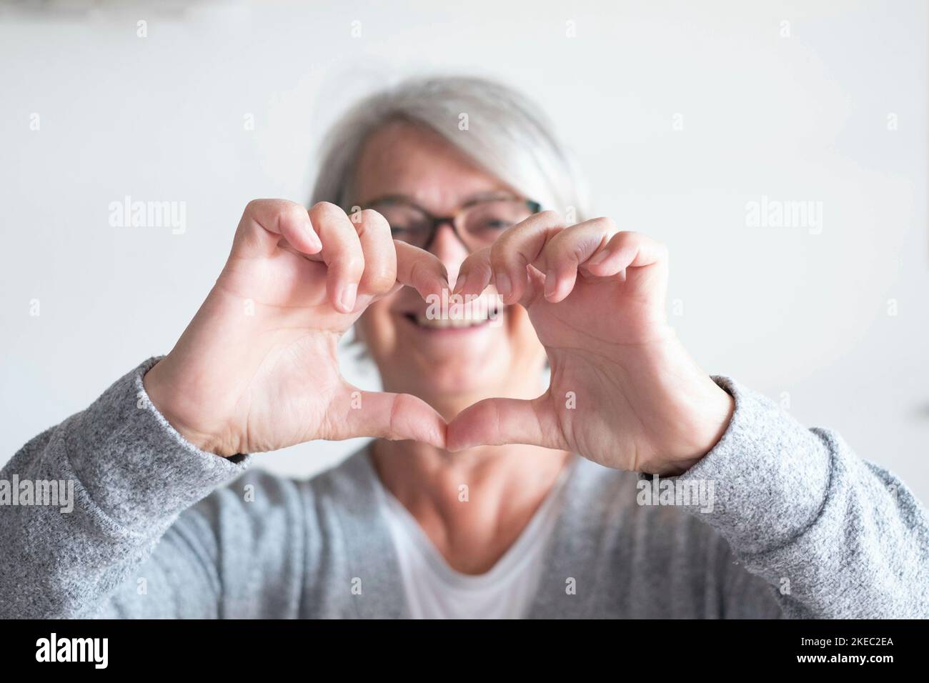 Eine reife Frau oder ein älterer zu Hause, die ein Herz tut Mit ihren Händen und Fingern - glücklicher Rentner Stockfoto