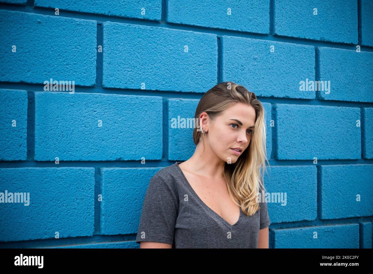 Nahaufnahme und Porträt der schönen blonden Frau mit blau Augen - Modell posiert mit einer blauen Wand an der Hintergrund Stockfoto