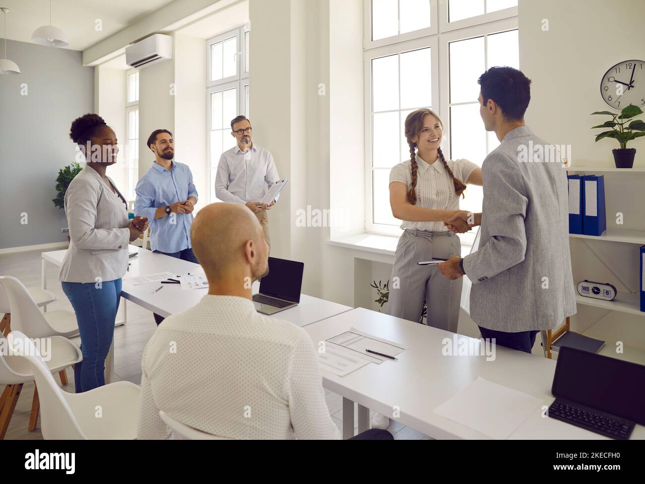 Mann und Frau grüßen sich gegenseitig und schüttelten die Hände und ihre Kollegen schauten sie im Büro an. Stockfoto