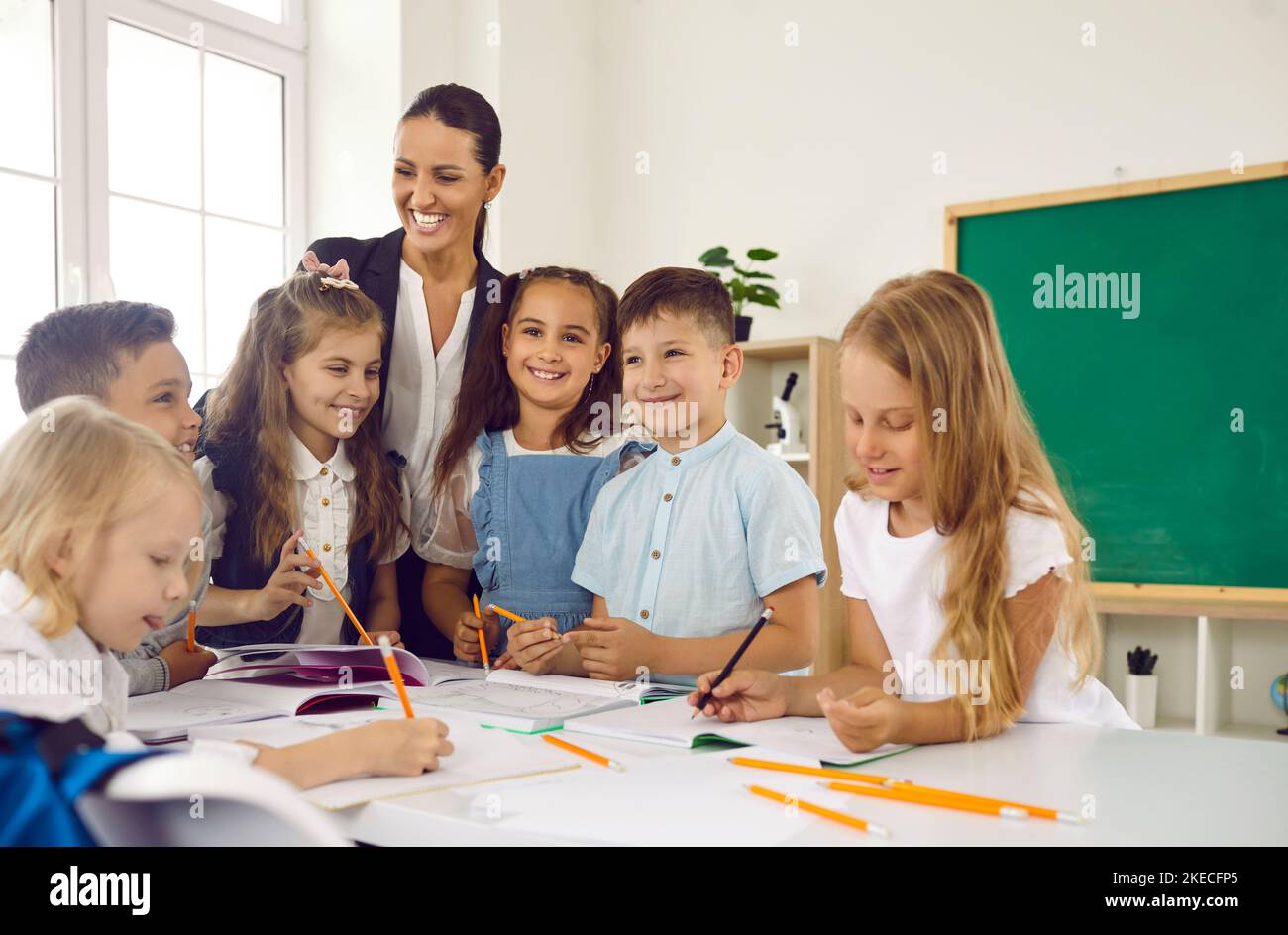 Glückliche kleine Kinder lernen zeichnen in der Grundschule stehen im Klassenzimmer mit Frau Lehrerin Stockfoto