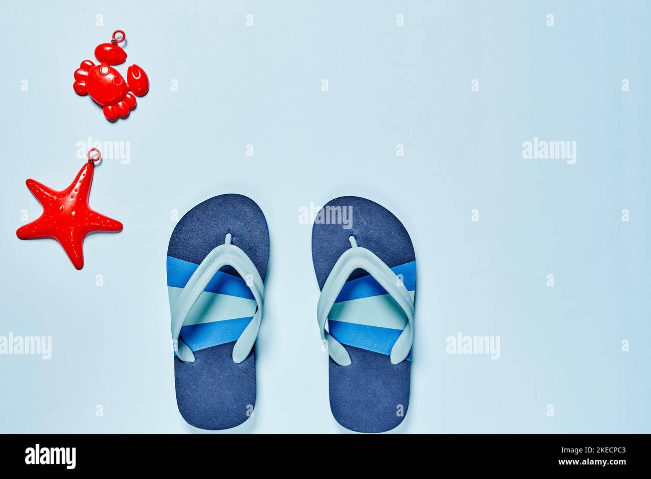 Zwei Paar blaue Flipflops und ein rotes Seesterne-Spielzeug auf weißem Hintergrund mit Platz für Text Stockfoto