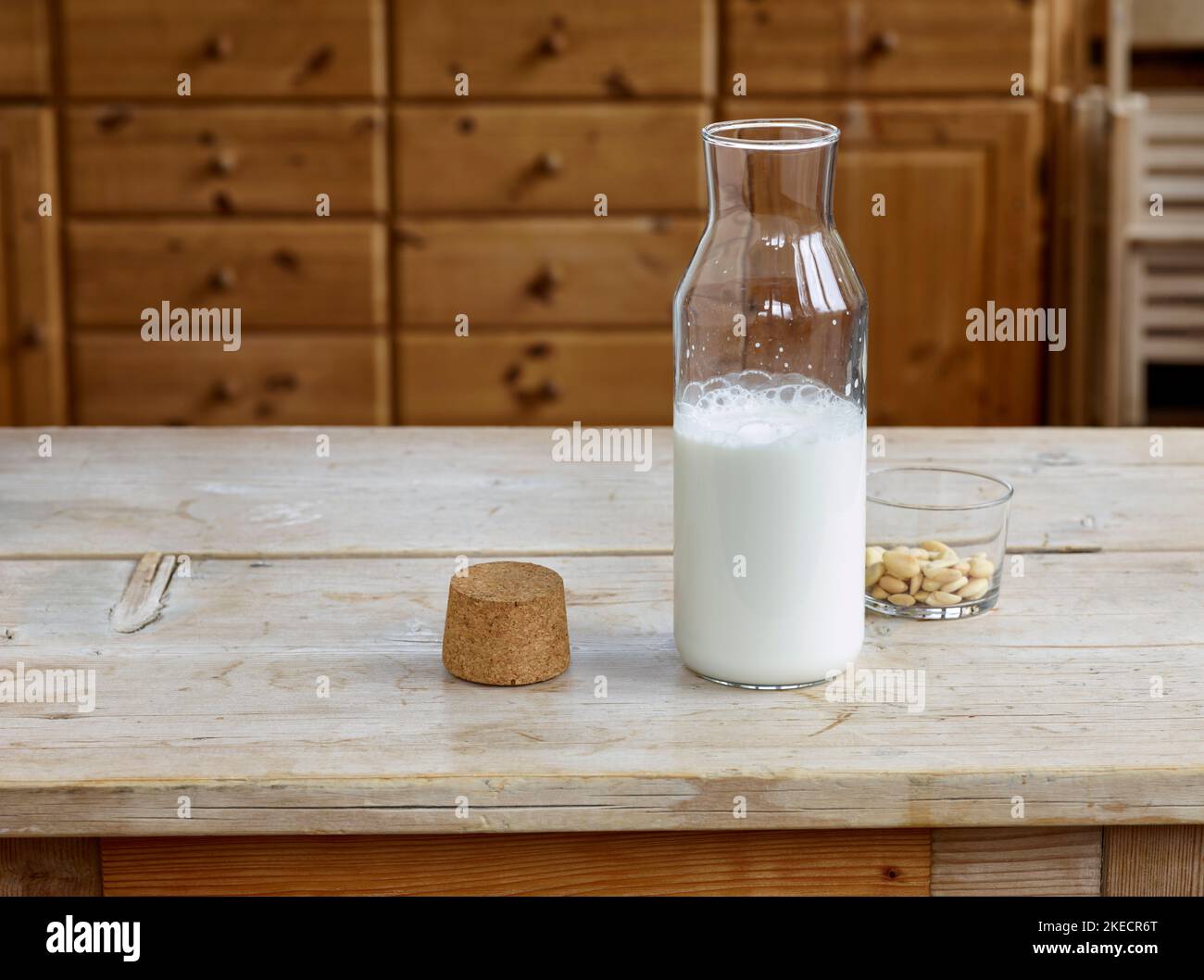 Schritte für die Herstellung von Mandelmilch, fertige Mandelmilch in einer Glasflasche mit Kork und einer Glasschale mit blanchierten Mandeln auf einem Holztisch Stockfoto