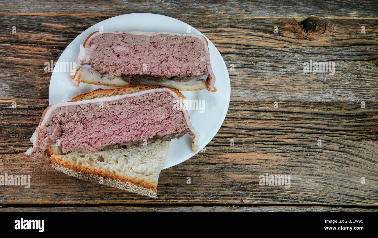 Hausgemachte Pastete, eingewickelt in Speck aus Schweinefleisch und Leber, auf einem rustikalen Tisch Stockfoto