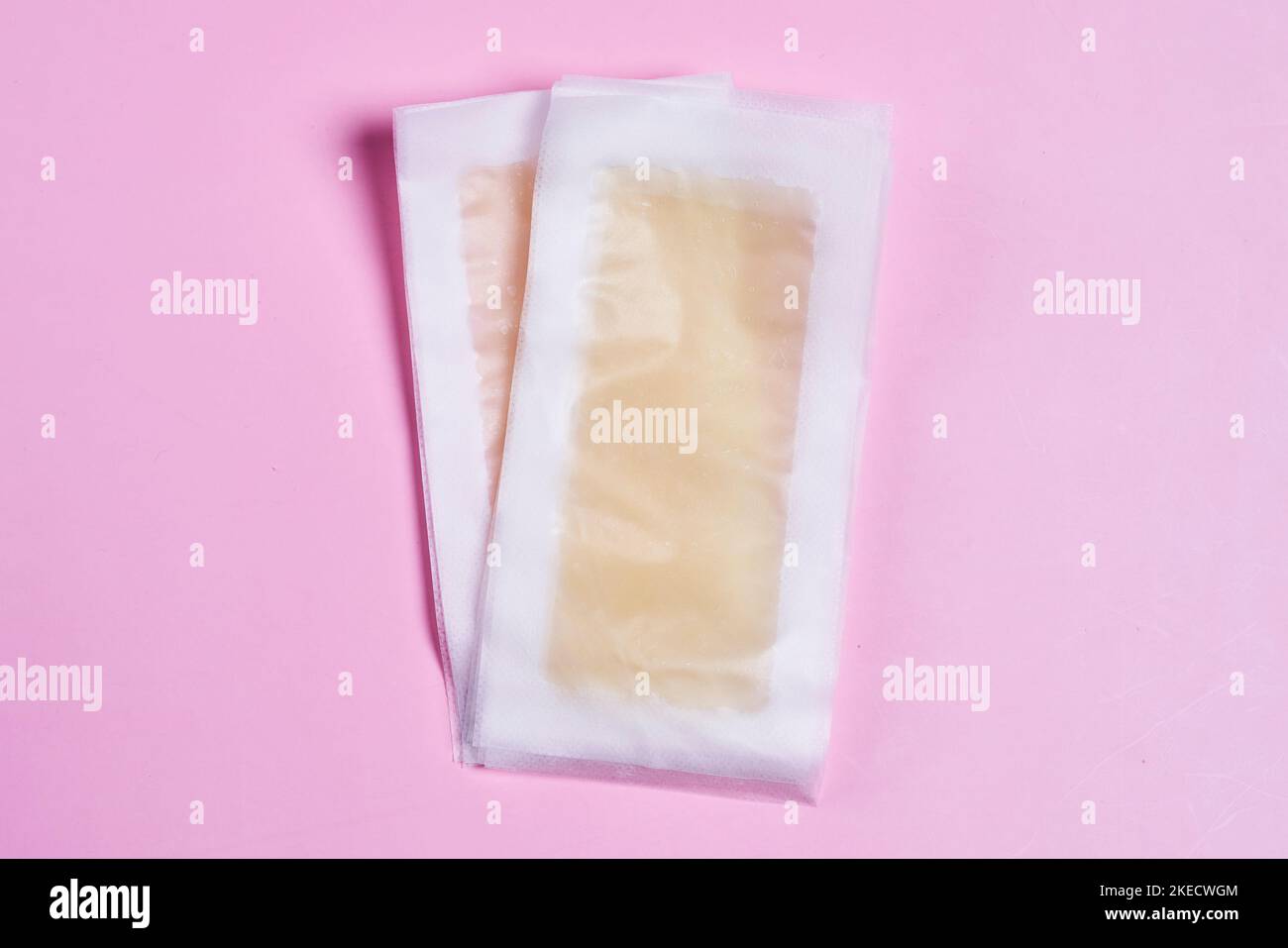 Zwei Eisstücke auf einem rosa Hintergrund, eines ist gefroren und das andere wird in Plastiktüten ausgepackt Stockfoto