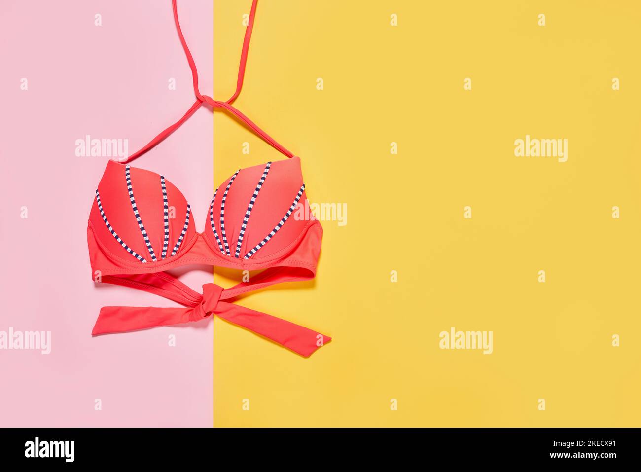 Ein Bikinitop auf einem gelben und rosa Hintergrund mit Kopie - Platz unten rechts liest handgeschriebener Text Stockfoto
