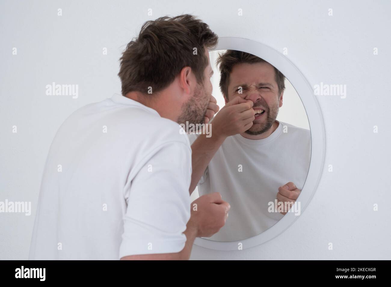 Ein Mann, der in den Spiegel schaut, berührt das Gesicht mit einem Pickel am Wangenknochen und fühlt sich verärgert. Stockfoto