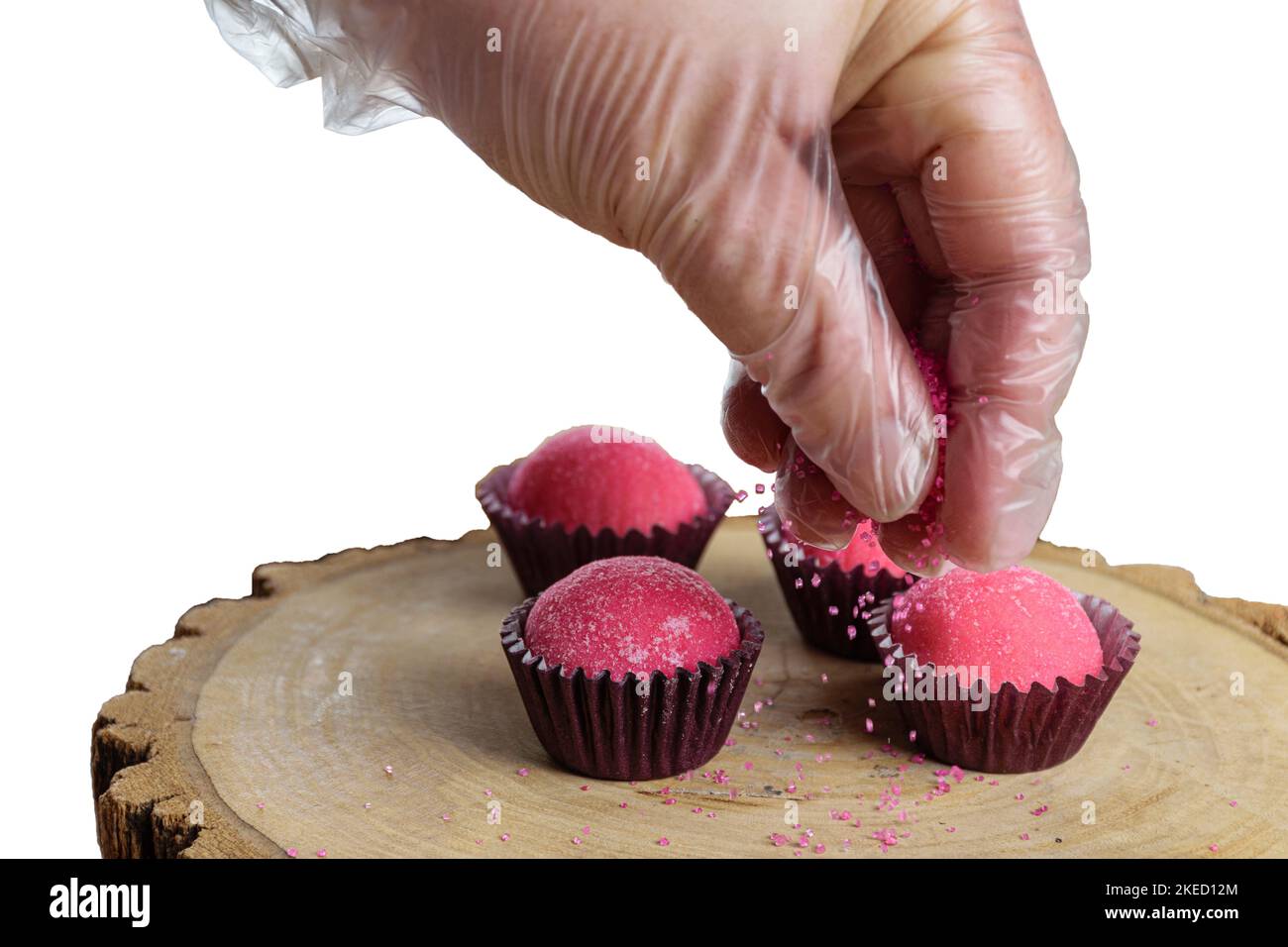 Erdbeer-Fudge-Kugeln (Bicho de PE) auf Baumstammschalen. Konditor setzt rosa Kristall Zucker weiß Hintergrund. Stockfoto