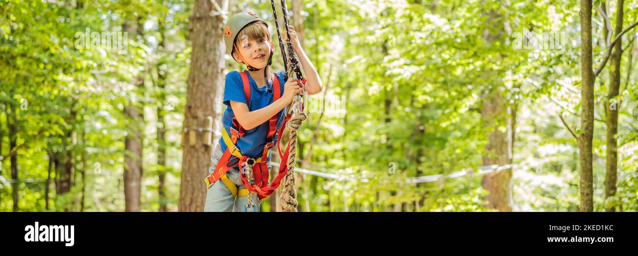 BANNER, LANG FORMAT glückliches Kind im Helm, gesunder Teenager Schuljunge, der an einem Sommertag in einem Kletterabenteuer-Park aktiv ist Porträt eines Stockfoto