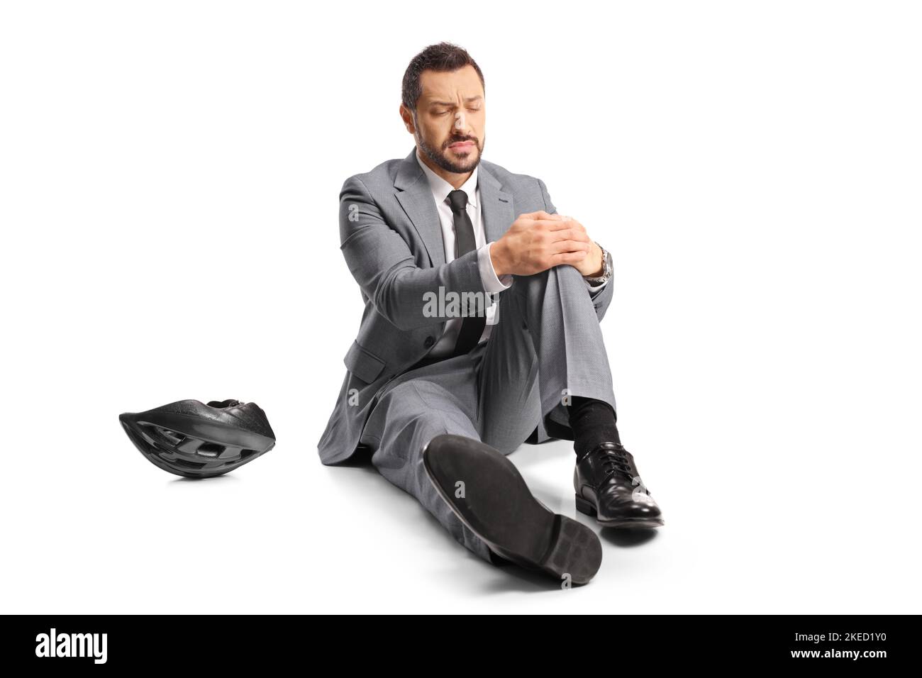 Geschäftsmann sitzt auf dem Boden und hält sein schmerzhaftes Knie isoliert auf weißem Hintergrund Stockfoto