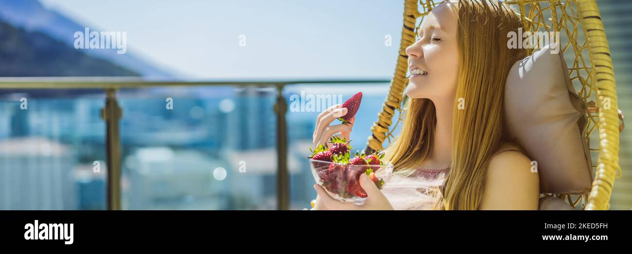 Portrait einer wunderschönen Frau in einem schönen Kleid auf einer Terrasse sitzen und essen Erdbeer-BANNER, LANG FORMAT Stockfoto