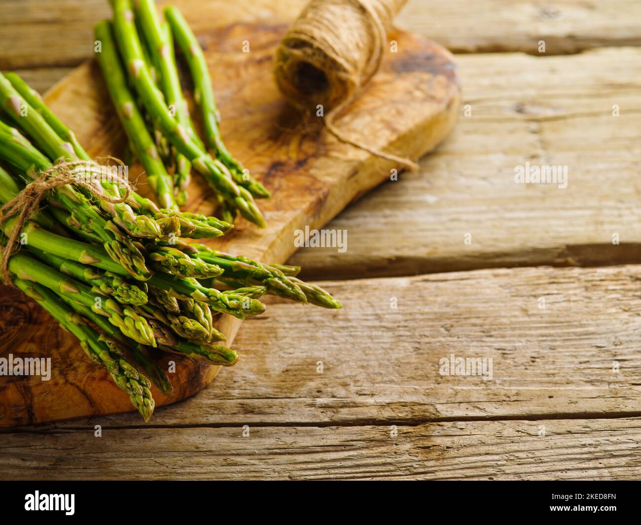 Frischer Spargel auf einem Schneidebrett und ein Garnstrang auf einem hölzernen Hintergrund. Vitamine, Antioxidantien. Gesunde Bio-Lebensmittel. Es gibt freien Platz für mich Stockfoto