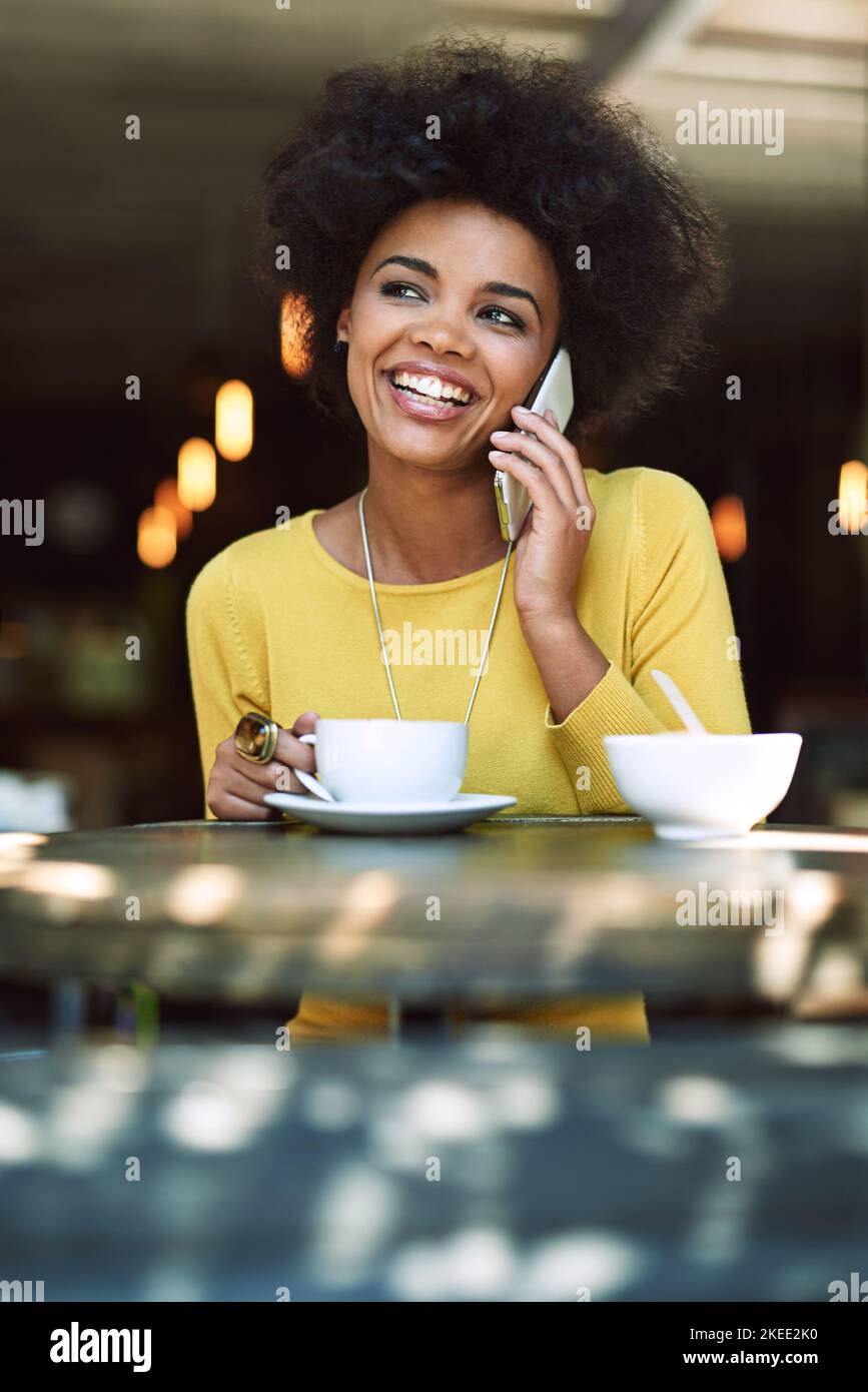 Ich genieße gerade eine schnelle Tasse Kaffee. Eine junge Frau, die in einem Café auf einem Handy spricht. Stockfoto