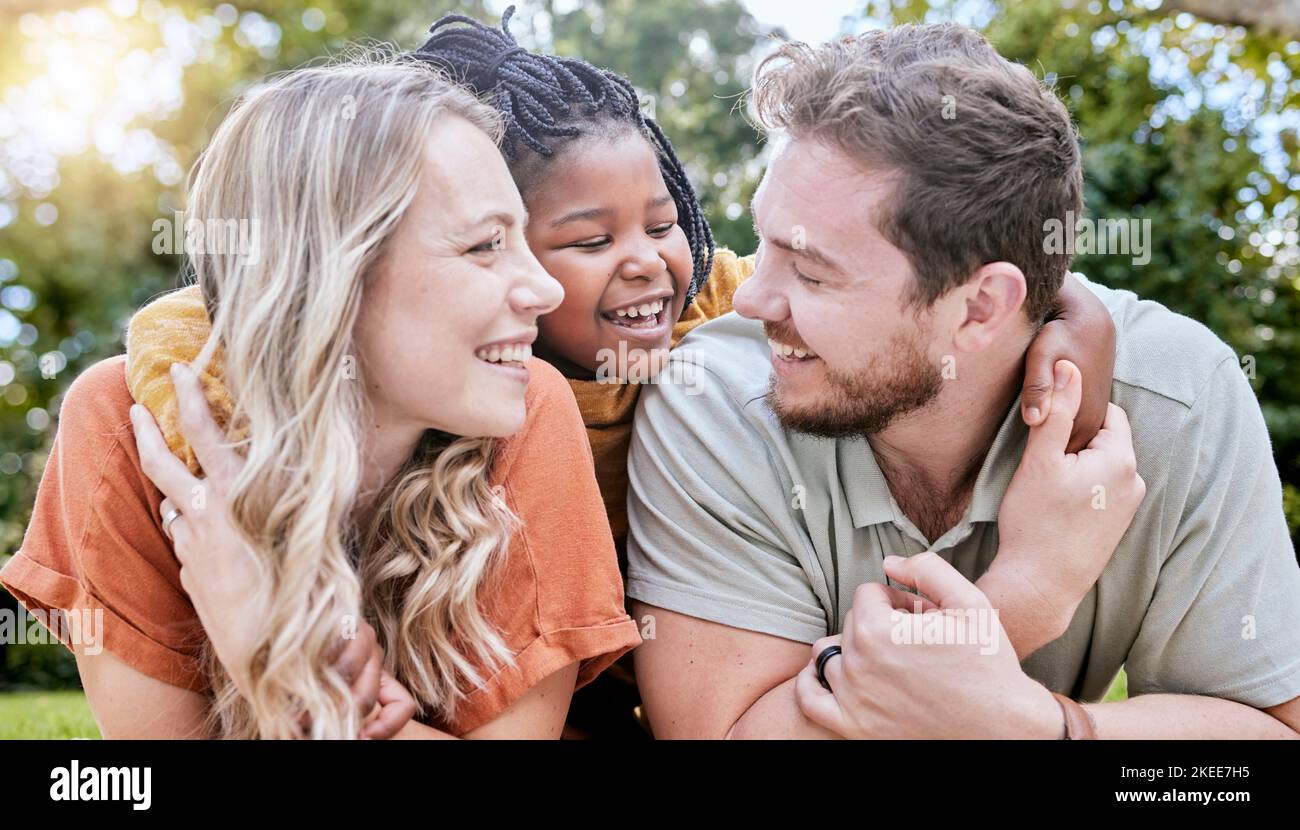 Glückliche Familie, Adoption und Kind umarmen Eltern, während sie sich entspannen, sich verbinden und die Zeit im Freien auf dem Parkgelände genießen. Liebe, Elternschaft und Stockfoto