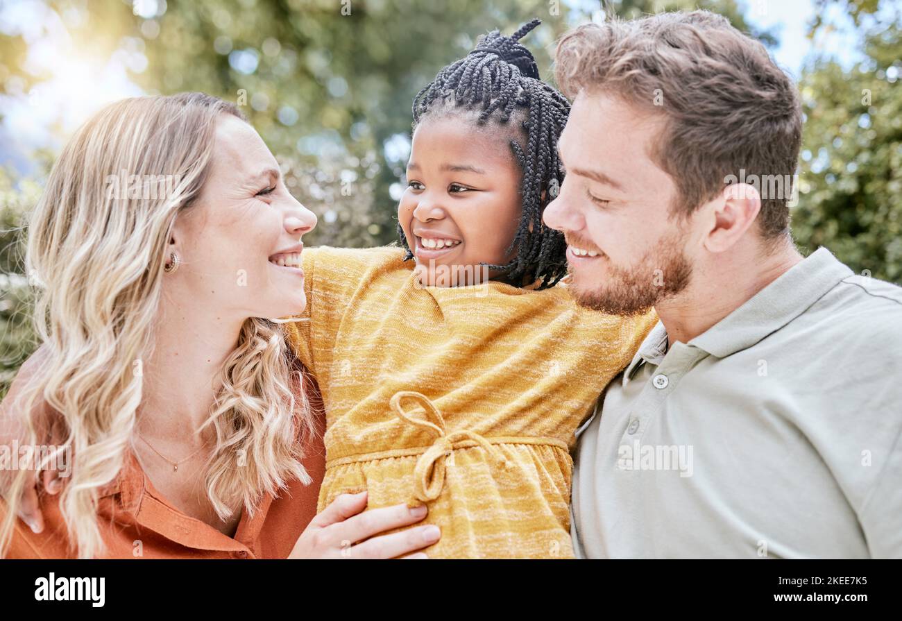 Adoption, Umarmung und Kind mit Eltern in einem Park mit Liebe, Lächeln und glücklich für interracial Familie. Glück, natürliche und afrikanische Mädchen Kind umarmt sie Stockfoto