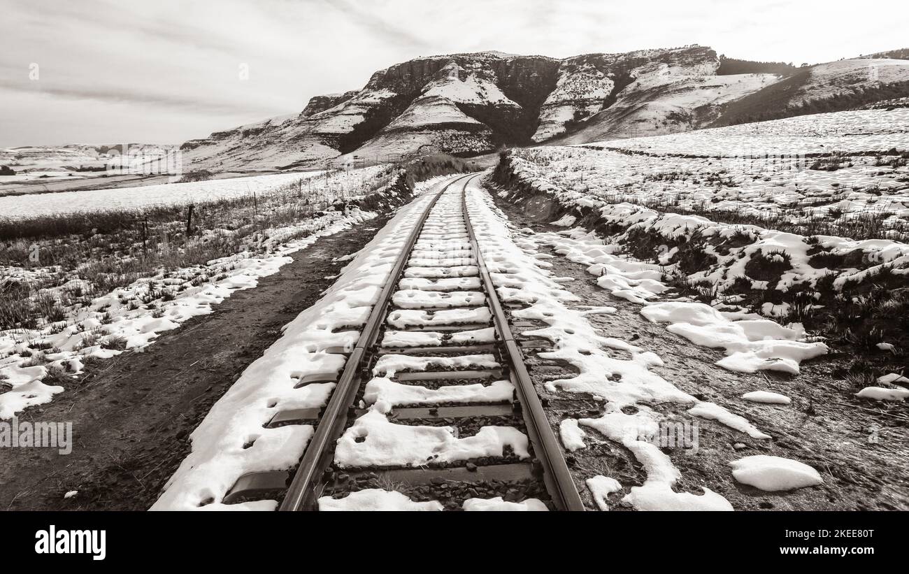 Bahngleise in ländlichen Bergen, die mit Winterschnee bedeckt sind, sind in der Nähe einer malerischen, schwarz-weißen, kontrastierenden Reiselandschaft mit Sepia. Stockfoto