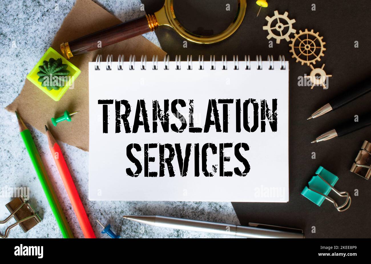 Auf einem Holztisch befinden sich Berichte, eine Topfpflanze, eine Lupe, ein schwarzer Stift und ein Notizbuch mit den ÜBERSETZUNGSDIENSTEN. Geschäftsbetrieb Stockfoto
