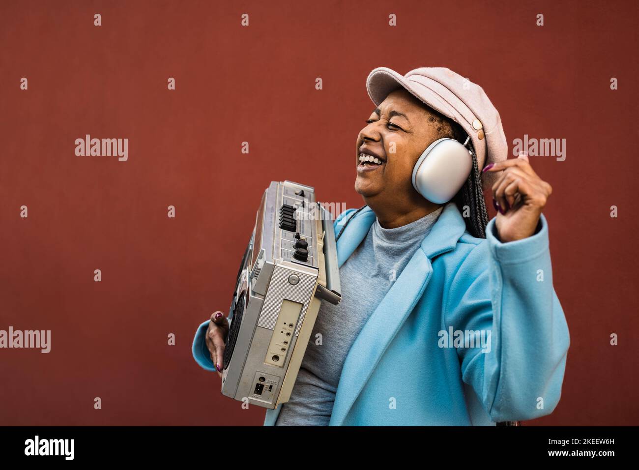 Fröhliche trendige ältere afrikanische Frau, die Spaß beim Tanzen hat, während sie Musik mit Kopfhörern und Vintage Boombox Stereo hört Stockfoto