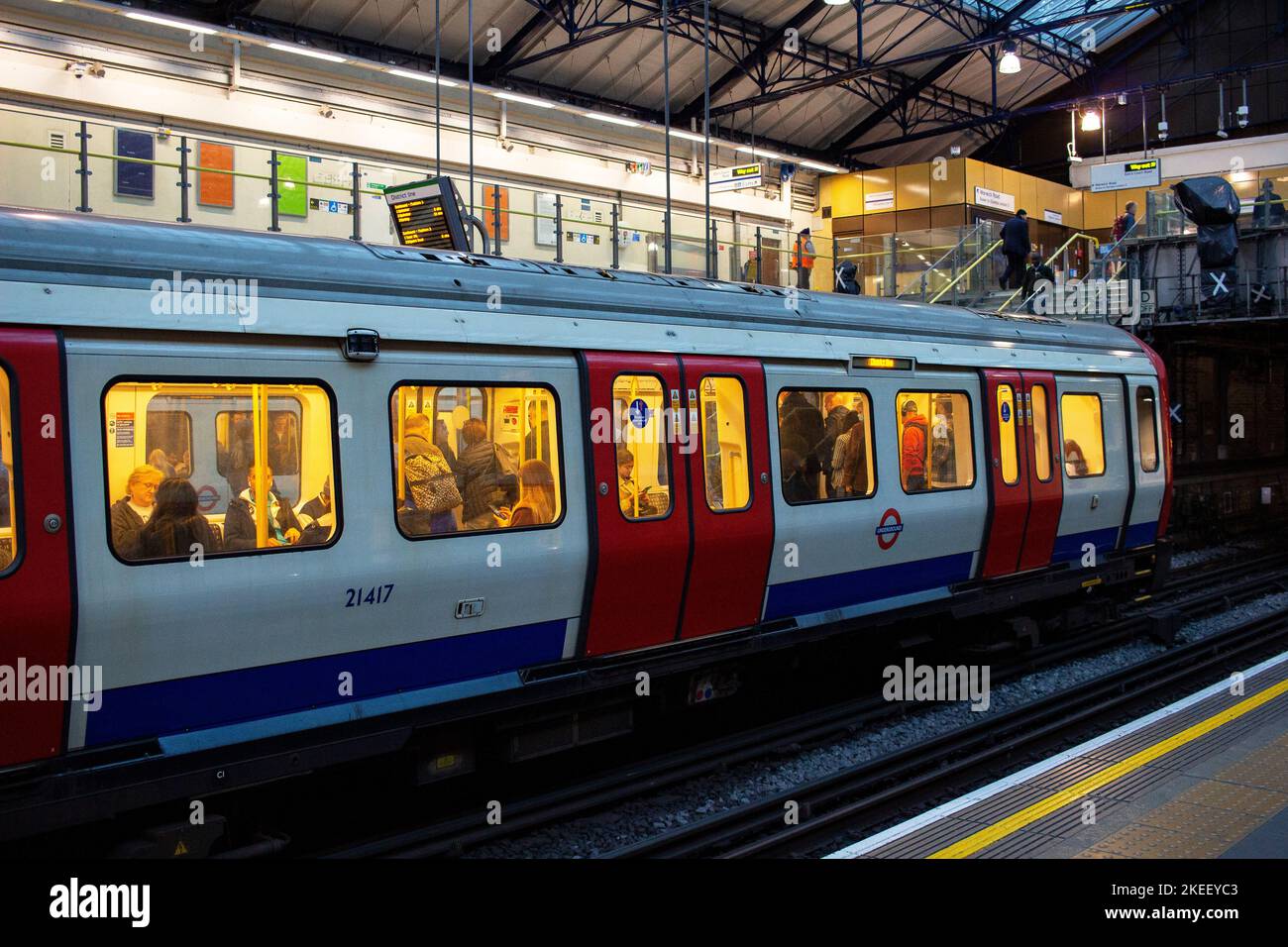 Londoner U-Bahn (The Tube); ein Zug der District Line hält in der Abenddämmerung an der Earls Court Station, die Wagenbeleuchtung zeigt den Passagieren das Innere Stockfoto