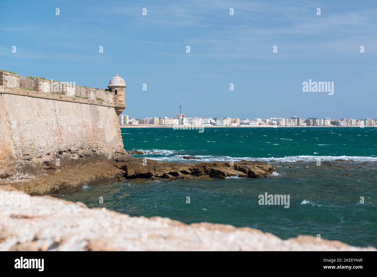 Die Mauern von Castillo de San Sebastián, Cádiz, Spanien, befinden sich auf einer kleinen Insel, die von der Hauptstadt getrennt ist und im Hintergrund sichtbar ist. Stockfoto