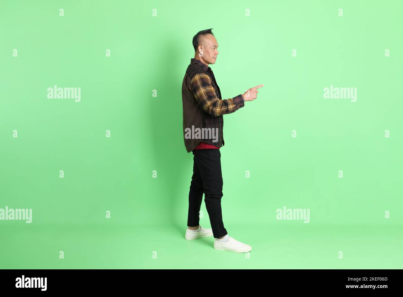 Der 40s-jährige asiatische Mann mit karierten Hemd auf grünem Hintergrund. Stockfoto