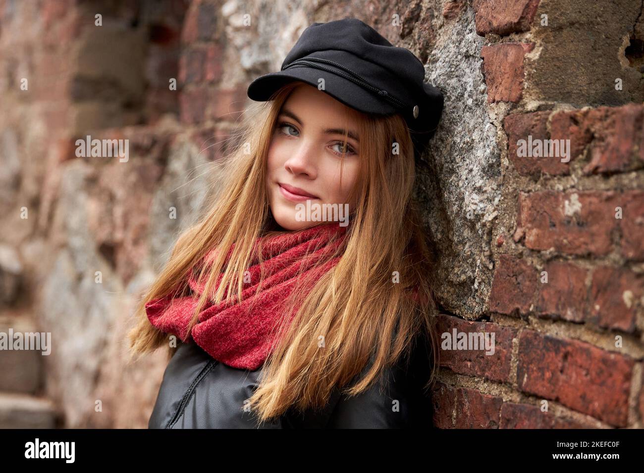 Mädchen in einer schwarzen Mütze mit einem roten Schal an einer Ziegelwand. Hochwertige Fotos Stockfoto