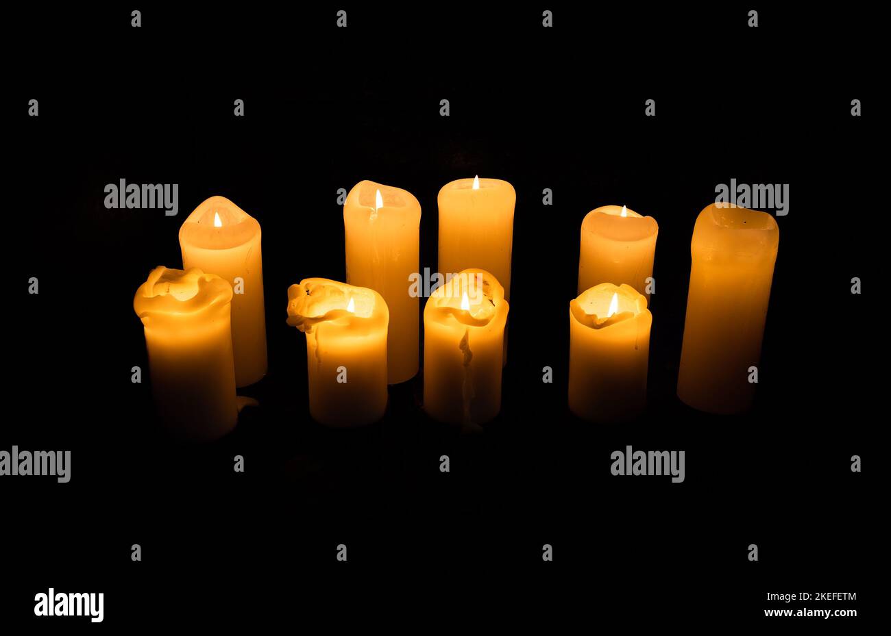 Eine Gruppe von neun brennenden Wachskerzen mit schwarzem Hintergrund Stockfoto