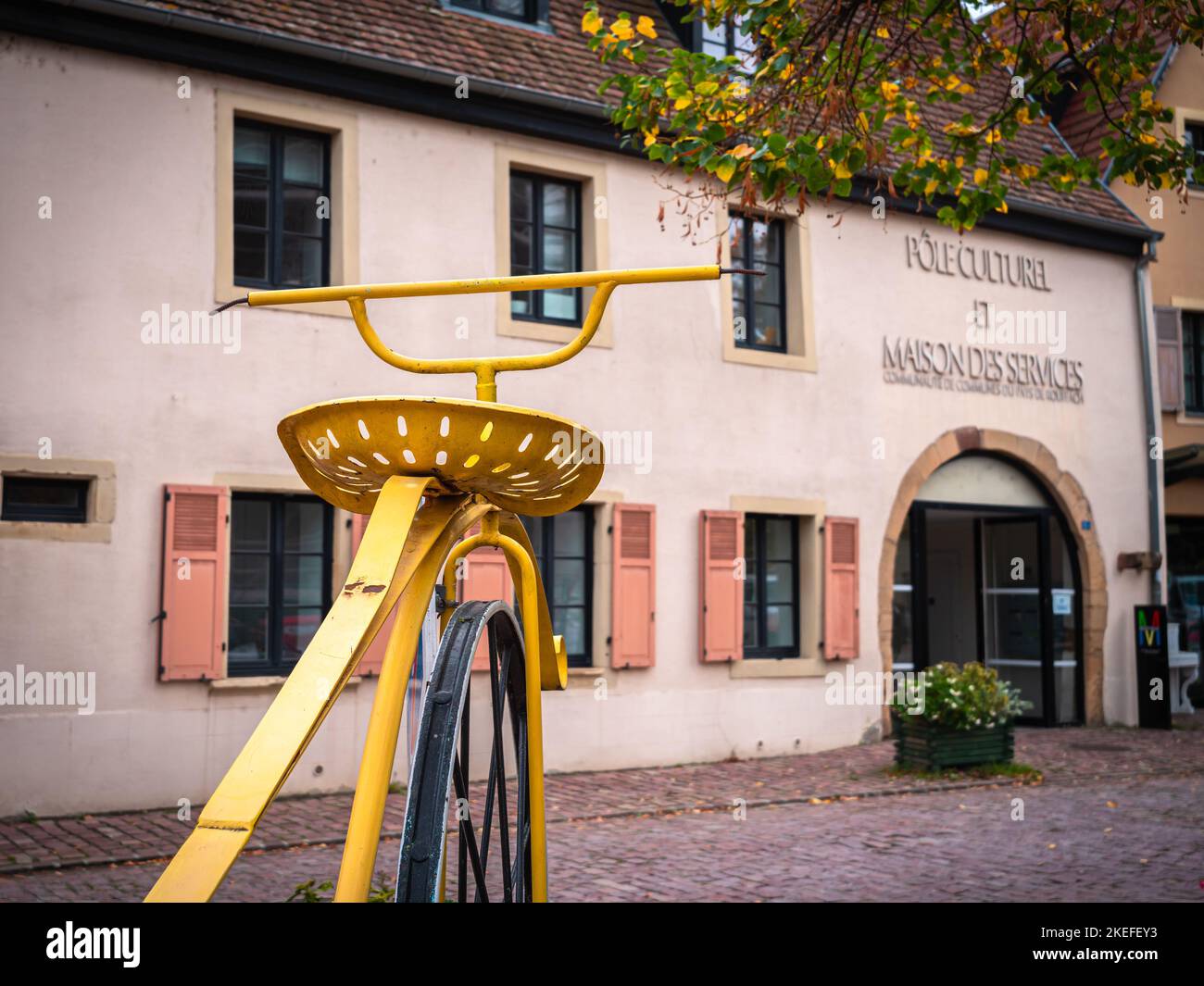 Rouffach, Frankreich - 11. Oktober 2022: Ein großes historisches gelbes Fahrrad vor einem Kultur- und Dienstleistungszentrum in Rouffach, Elsass Stockfoto