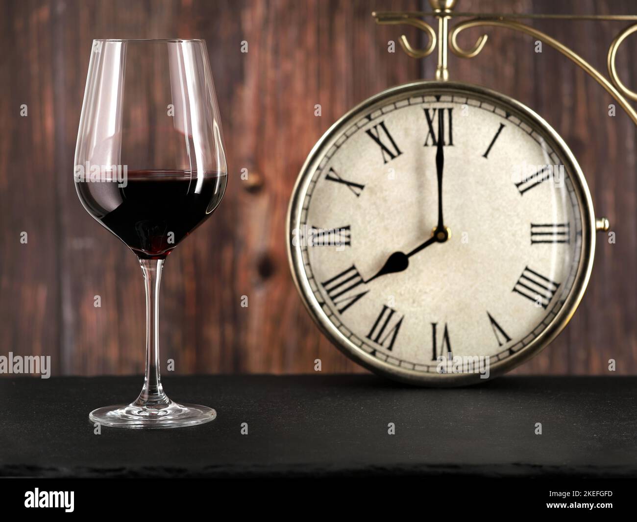 Glas Rotwein mit antiker Uhr auf Holzhintergrund, Konzeptbild für das Abendessen oder Alkoholismus am Abend nach der Arbeit Stockfoto