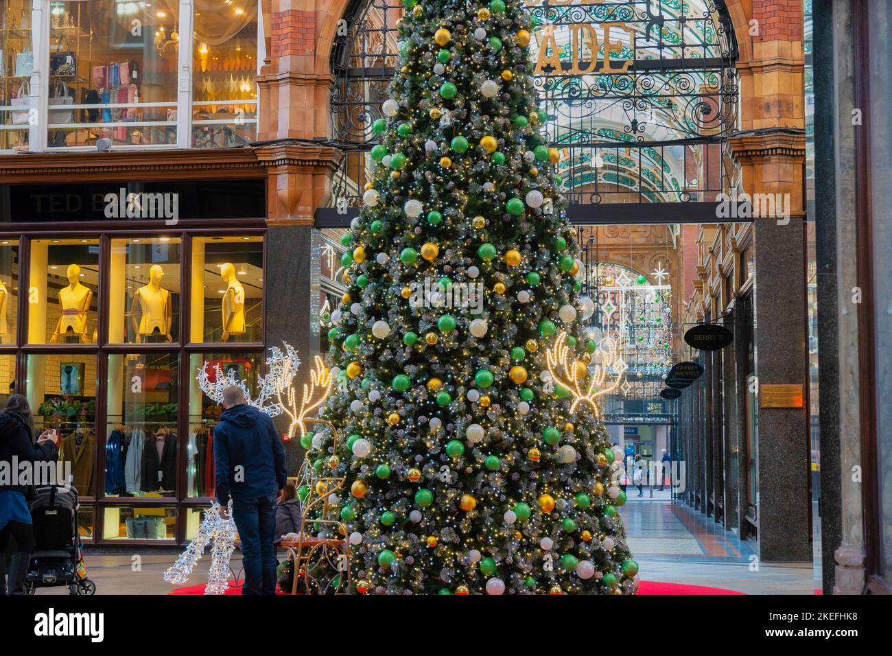 In einer Einkaufspassage im Victoria Quarter, Leeds, England, stand ein Einkäufer neben einem hohen Weihnachtsbaum, der mit großen Kugeln dekoriert war. Stockfoto