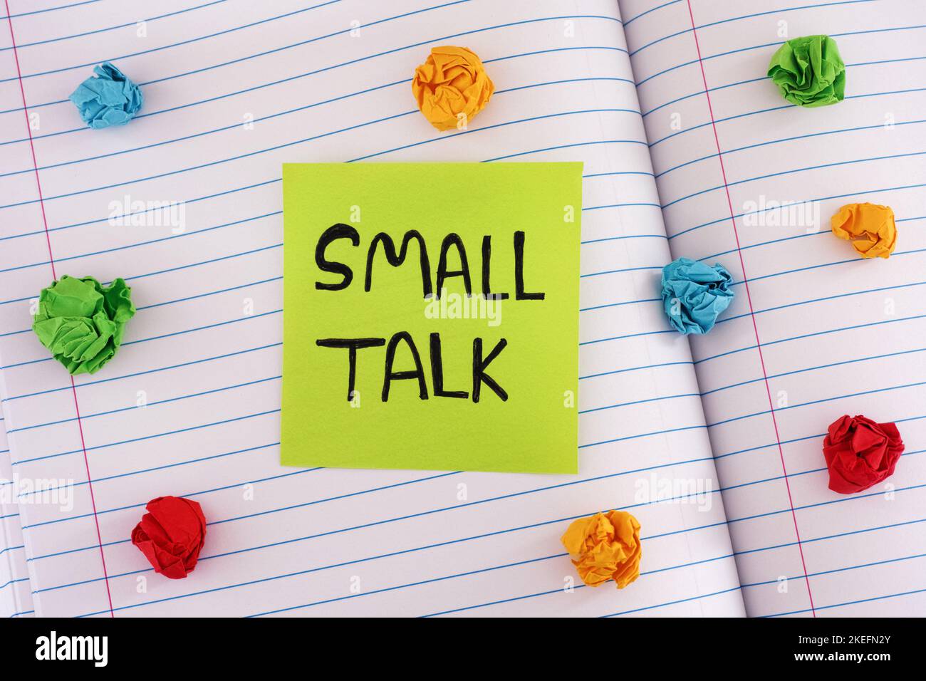 Eine grüne Papiernotiz mit den Worten Small Talk auf einem Notizbuch mit einigen bunten zerknitterten Papierkugeln um sie herum. Nahaufnahme. Stockfoto